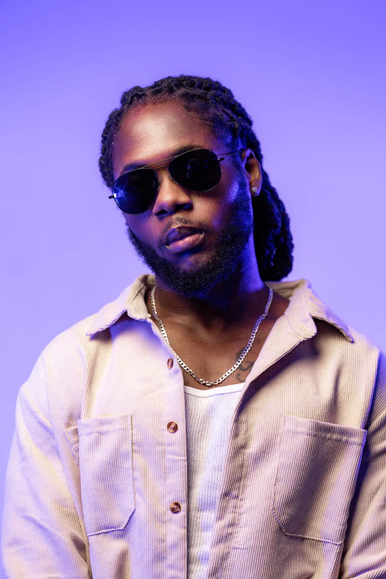 Saint Chris seated campaign portrait with sunglasses and cream overshirt.